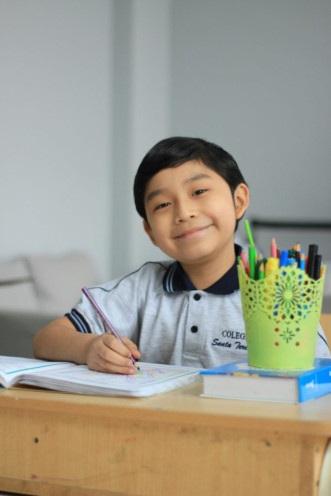 Young boy in school uniform doing homework with colored pencils indoors.